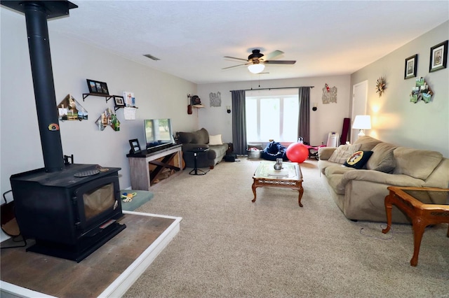 living room with ceiling fan, carpet floors, and a wood stove