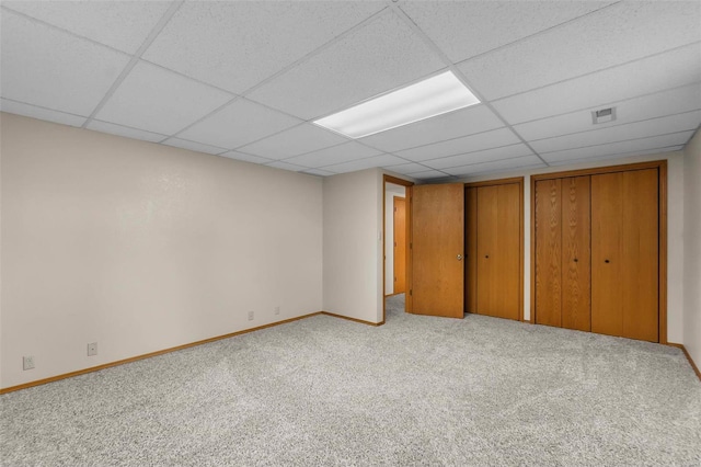 unfurnished bedroom featuring two closets, a paneled ceiling, and carpet flooring