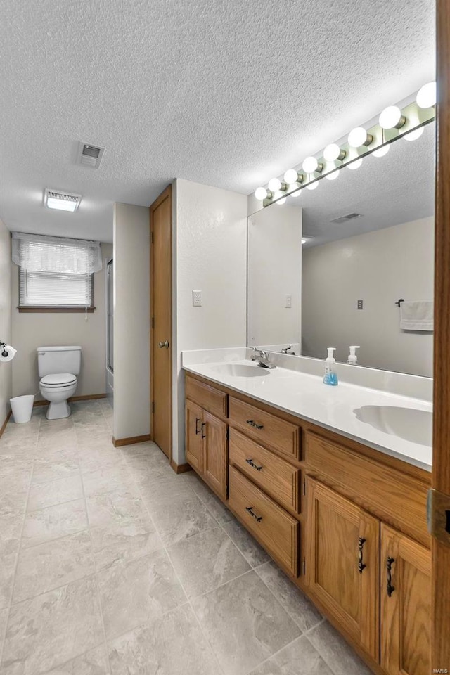 bathroom with dual vanity, tile patterned floors, a textured ceiling, and toilet