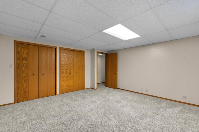 unfurnished bedroom with a paneled ceiling, two closets, and carpet floors