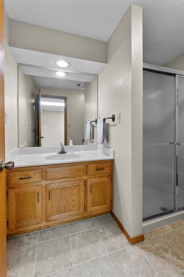 bathroom featuring a textured ceiling, vanity, a shower with shower door, and tile patterned flooring