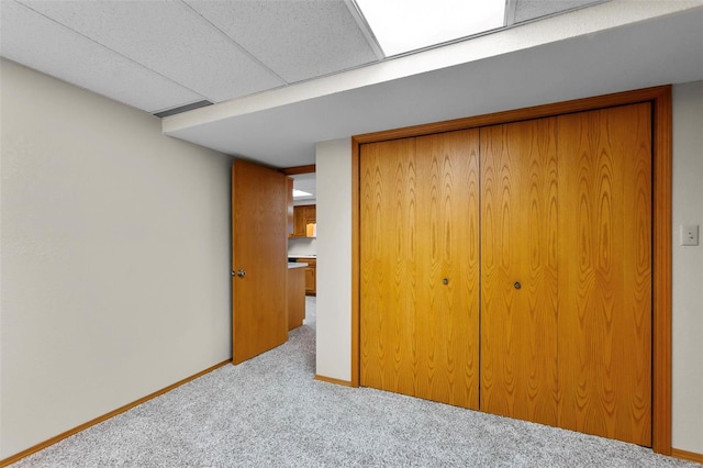 unfurnished bedroom with a paneled ceiling, light carpet, and a closet