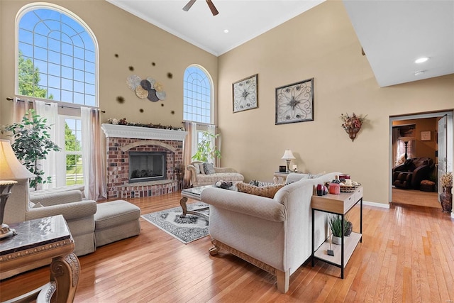 living room featuring a high ceiling, a fireplace, light hardwood / wood-style floors, ornamental molding, and ceiling fan