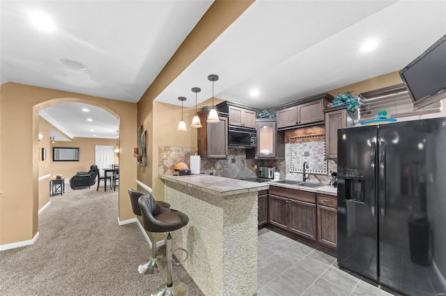 kitchen featuring backsplash, decorative light fixtures, black appliances, sink, and light colored carpet