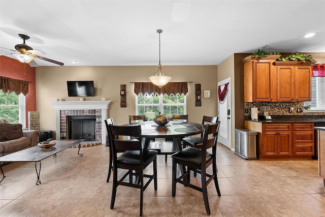 tiled dining space with ceiling fan, plenty of natural light, and a brick fireplace