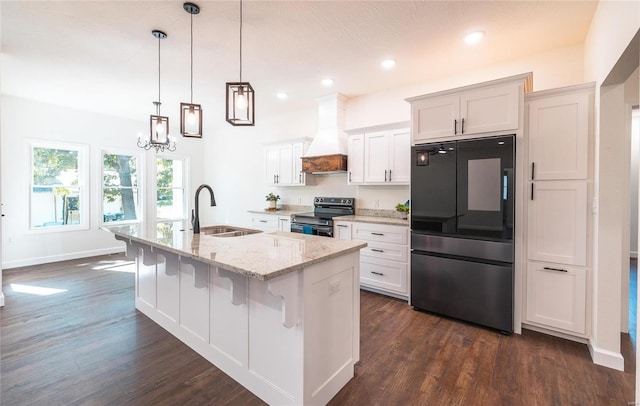 kitchen featuring an island with sink, black appliances, white cabinets, premium range hood, and sink