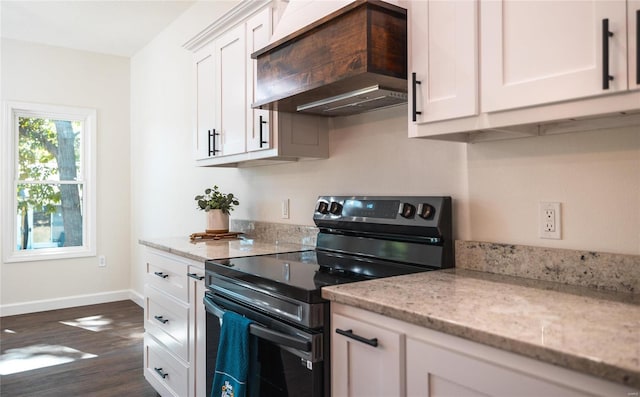 kitchen with light stone countertops, white cabinets, black electric range oven, and premium range hood