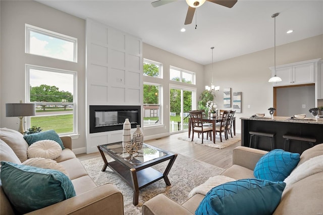 living room featuring light hardwood / wood-style floors, ceiling fan with notable chandelier, and a large fireplace