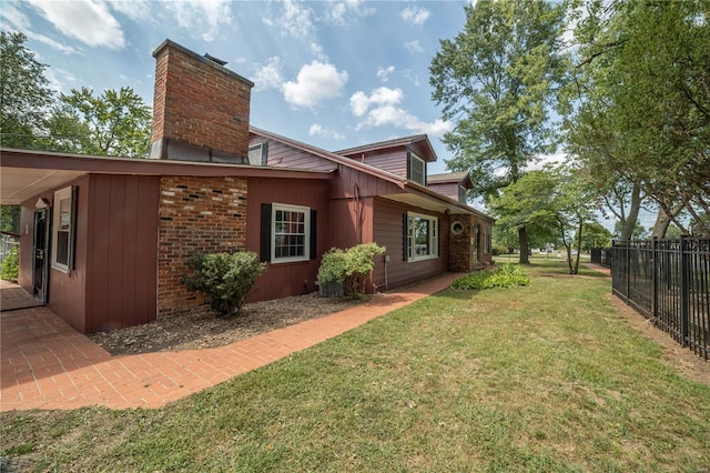 view of home's exterior featuring brick siding, fence, a chimney, and a lawn