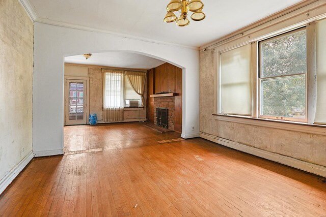 unfurnished living room featuring crown molding, a brick fireplace, a baseboard heating unit, wood-type flooring, and a chandelier