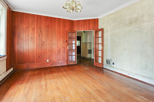 empty room with wood walls, an inviting chandelier, ornamental molding, and hardwood / wood-style floors