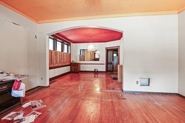 empty room with wood-type flooring, ornamental molding, and an inviting chandelier