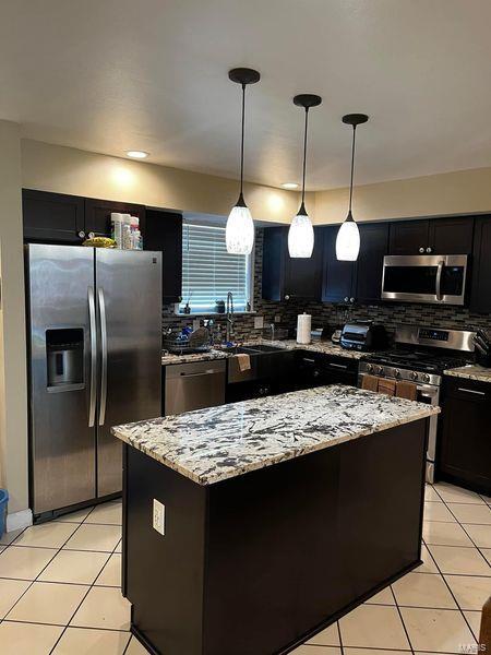 kitchen with light tile patterned floors, appliances with stainless steel finishes, hanging light fixtures, and backsplash