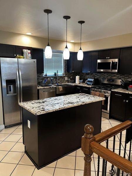 kitchen with pendant lighting, a kitchen island, tasteful backsplash, light tile patterned floors, and stainless steel appliances