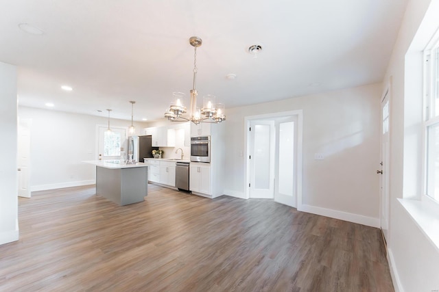 kitchen with pendant lighting, white cabinets, a center island with sink, appliances with stainless steel finishes, and hardwood / wood-style floors