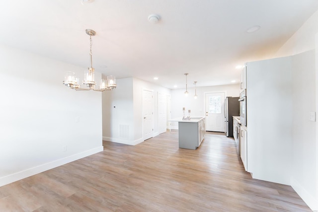 kitchen with pendant lighting, light hardwood / wood-style floors, an island with sink, white cabinetry, and stainless steel fridge