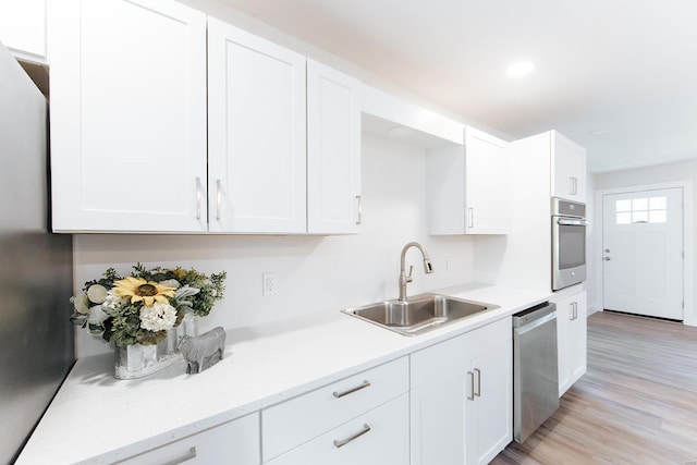 kitchen with appliances with stainless steel finishes, light wood-type flooring, white cabinetry, and sink