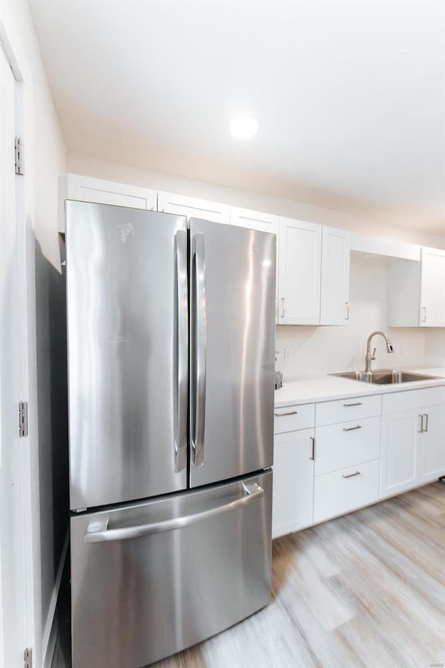 kitchen with white cabinets, light wood-type flooring, stainless steel fridge, and sink