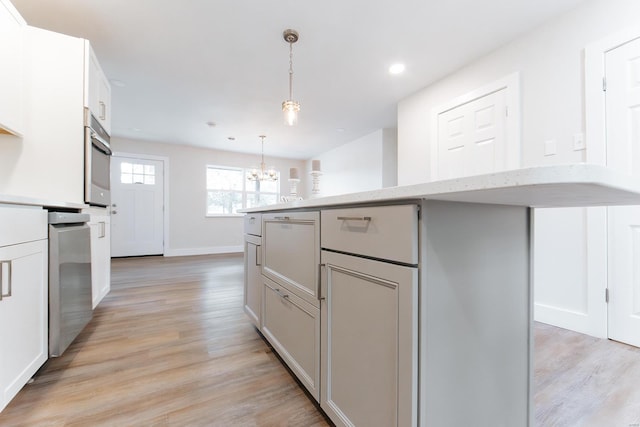 kitchen featuring light stone counters, pendant lighting, light hardwood / wood-style flooring, a center island, and an inviting chandelier