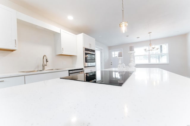 kitchen featuring pendant lighting, white cabinets, sink, appliances with stainless steel finishes, and an inviting chandelier