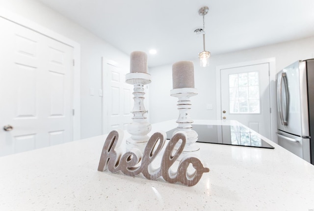 room details with light stone counters, stainless steel refrigerator, decorative light fixtures, and black electric stovetop