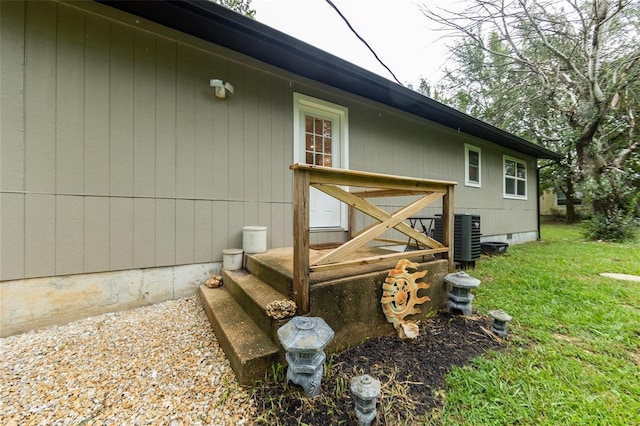 view of exterior entry featuring a lawn and central air condition unit