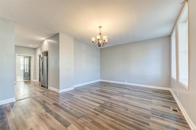 empty room featuring hardwood / wood-style flooring, an inviting chandelier, and plenty of natural light