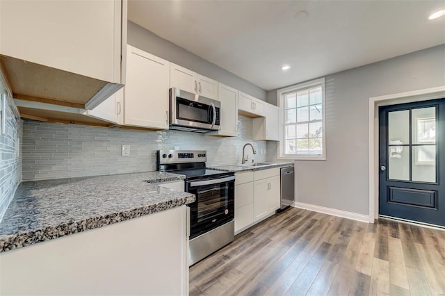 kitchen featuring tasteful backsplash, appliances with stainless steel finishes, white cabinetry, light stone countertops, and light hardwood / wood-style floors