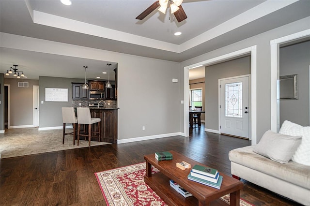 living room featuring ceiling fan, a raised ceiling, and dark hardwood / wood-style floors