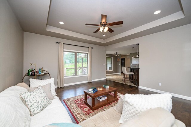 living room with a tray ceiling, ceiling fan, and dark hardwood / wood-style flooring