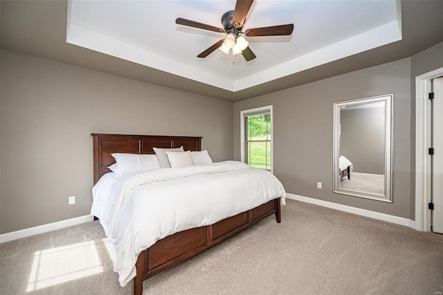 carpeted bedroom featuring a tray ceiling and ceiling fan