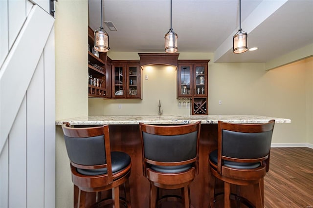 bar with light stone countertops, dark hardwood / wood-style flooring, and hanging light fixtures