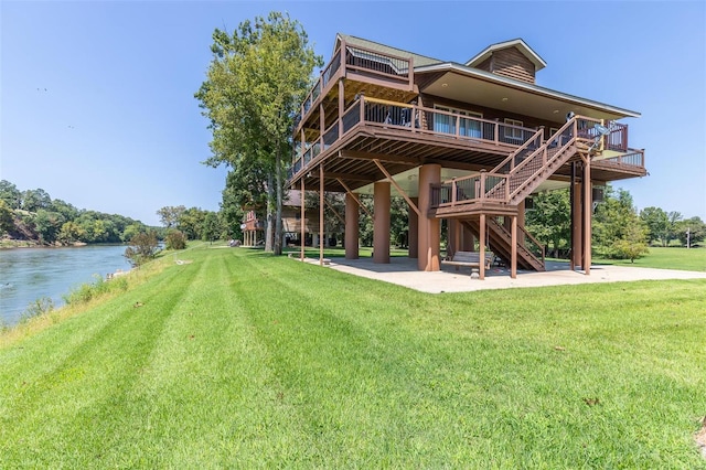 rear view of house with stairs, a yard, a patio, and a water view