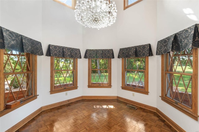 unfurnished dining area with a chandelier, a healthy amount of sunlight, parquet floors, and a high ceiling