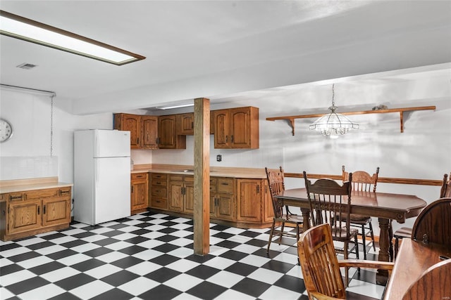 kitchen with hanging light fixtures, white fridge, backsplash, and an inviting chandelier