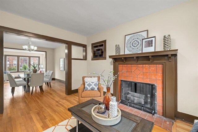 living room with a notable chandelier, a tiled fireplace, and wood-type flooring