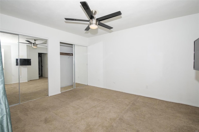 unfurnished bedroom with ceiling fan, light colored carpet, and two closets