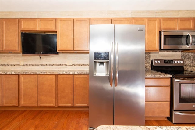 kitchen with decorative backsplash, light stone countertops, stainless steel appliances, and light wood-type flooring