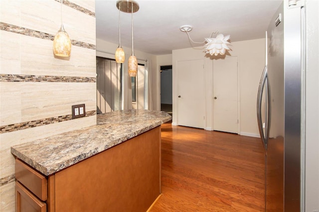 kitchen with light stone counters, wood-type flooring, hanging light fixtures, and stainless steel refrigerator