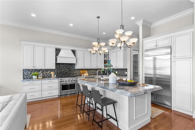 kitchen featuring hardwood / wood-style flooring, custom exhaust hood, a center island with sink, and high quality appliances