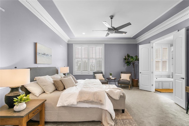 bedroom featuring ceiling fan, a tray ceiling, ensuite bath, carpet floors, and crown molding