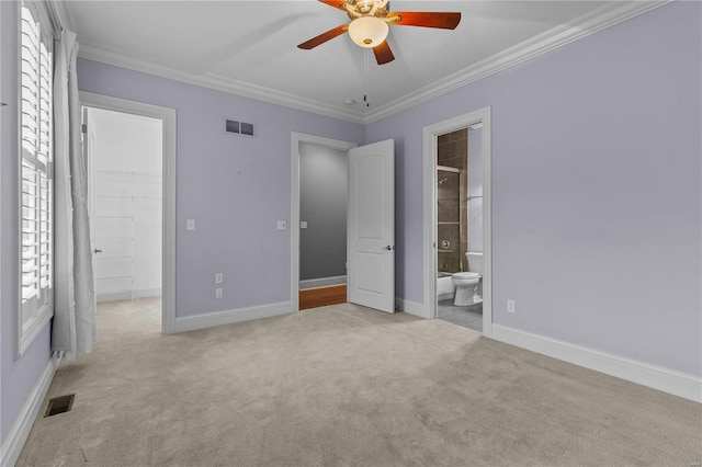 unfurnished bedroom featuring a walk in closet, crown molding, ceiling fan, light carpet, and ensuite bathroom