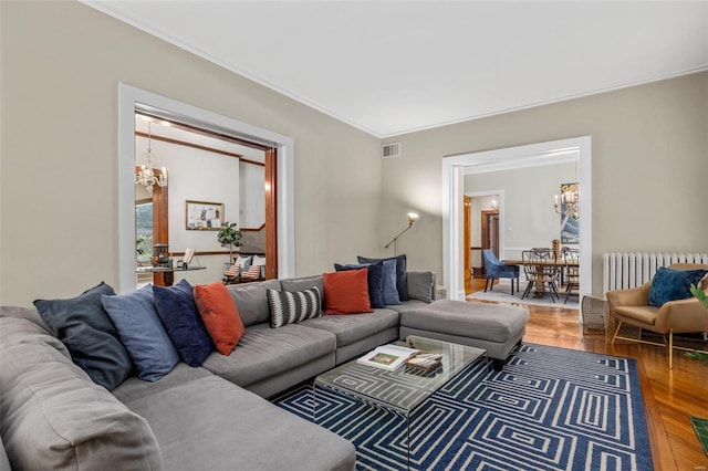 living room with wood-type flooring, a notable chandelier, ornamental molding, and radiator