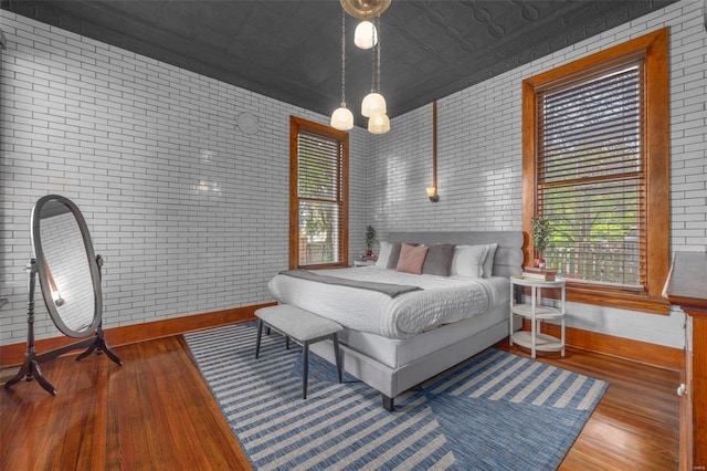 bedroom with brick wall, a notable chandelier, and wood-type flooring