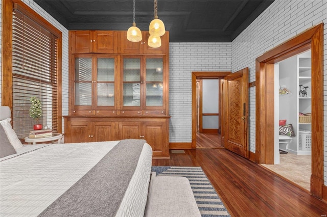 bedroom with dark wood-type flooring and brick wall