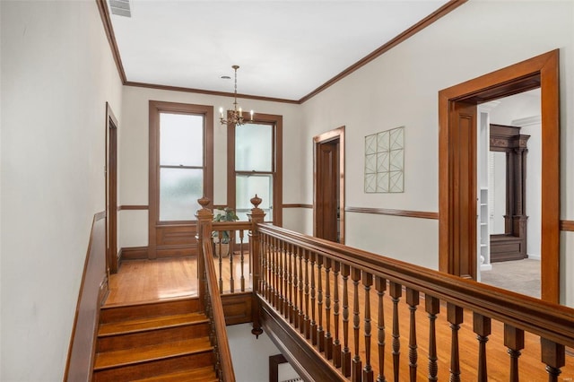 stairs with a notable chandelier, hardwood / wood-style floors, and ornamental molding