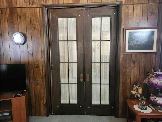 doorway to outside with wooden walls, french doors, and light colored carpet