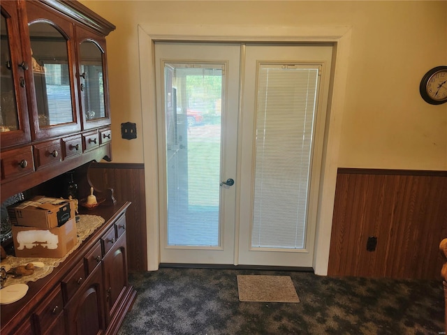 doorway to outside with wood walls, dark carpet, and french doors