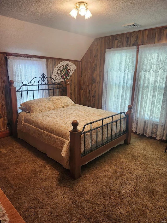 bedroom featuring dark carpet, a textured ceiling, ceiling fan, lofted ceiling, and wood walls