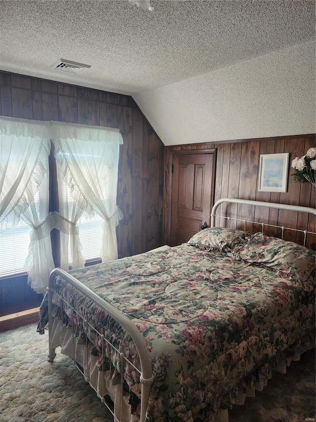 carpeted bedroom with a textured ceiling, lofted ceiling, and wood walls